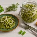 Saure Bohnen nach DDR-Rezept auf grünem Teller und im Einmachglas mit Zwiebeln, serviert auf hellem Holztisch mit Holzmaserung.